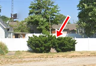 stone marker, flagpole, bushes behind, grassy shoulder in front