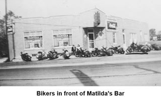 black and white 1950s photo, bar, single story on a corner, motorbikes by it, corner entrance with neon sign, US 66 runs in front