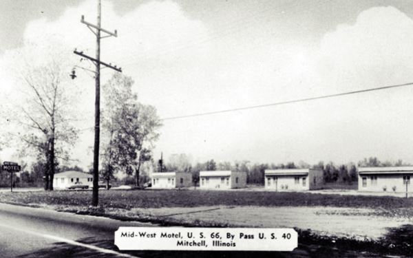 black and white 1940s postcard with cabins of a motel lined up facing Route 66
