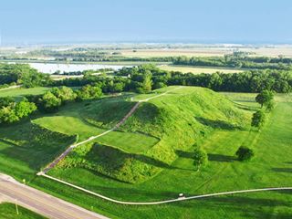 Monks Mound and US66 enormous mound covered with grass among trees seen from the air, Route 66 next to it