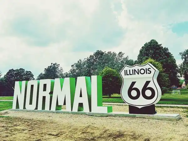 lawn, trees beyond, foreground: green and white capital letters spell NORMAL and a black and white US66 highway shield