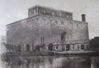 Norton Building 1873 Lockport IL 1873, black and white stone building 4 stories, a grain elevator, by a canal, with barge, men and suspension bridge
