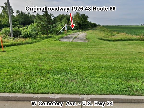 color, current view of a cracked concrete roadbed separated from a modern highway by a gap filled with grass, field to the right, trees to the left