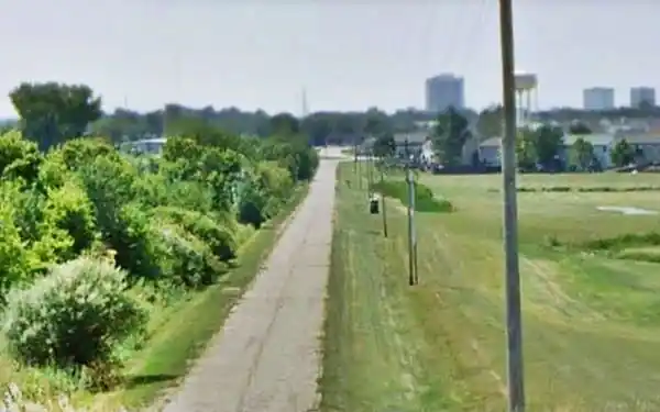 trees left, narrow highway center, field left, seen from a viaduct, buildings in the distance
