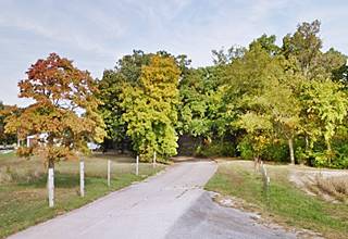 narrow concrete roadbed curves into some trees by a farm