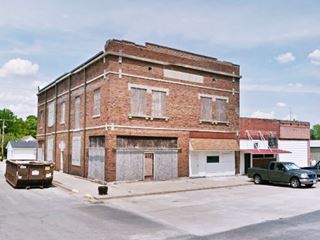 two story red brick building on a corner, boarded windows