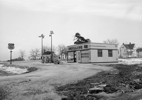 1950 black and white, box shaped Phillips 66 station, 3 gas pumps, sign, car parked