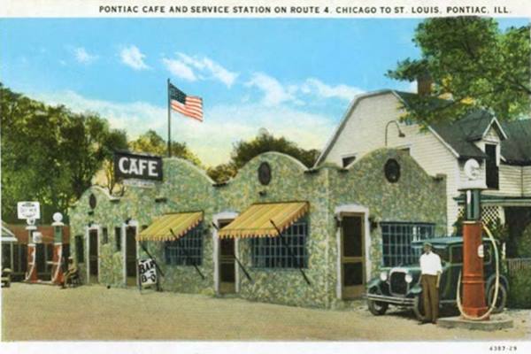color linnen postcard, man by stone building, a Cafe, gas pumps furhter down, wavy parapet on the bld. Woodframe 2 story home to the right