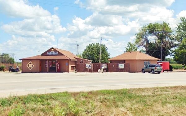 gable roof building cabin-like left, and hip roof building right. Highway runs in front