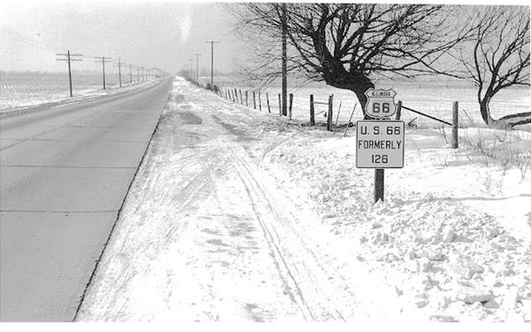 black and white c1940 snowed countryside sign by side of 2 lane concrete highway reads:US 66 -Shield- US66 FORMERLY 126