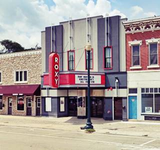 1930s theater with red marquee with white letters spelling ROXY, old buildings next to it