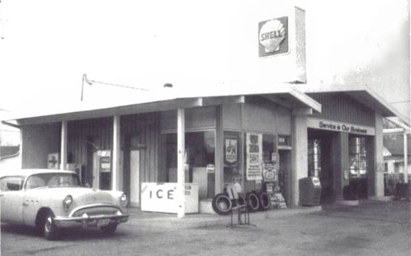 black and white Shell station, 2 gable roofs, chimney-like column with shield