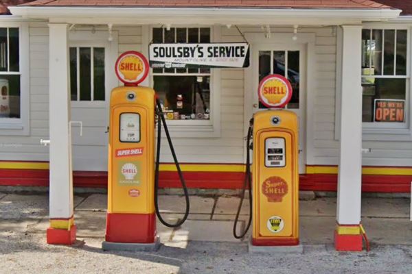 two old Shell gas pumps on an island under hipped roof canopy, office is behind them