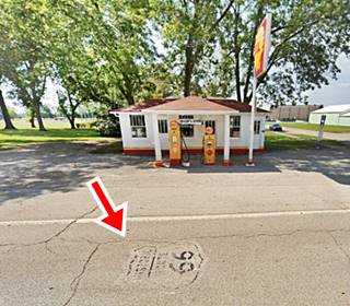 Route 66 shield painted on the roadway in front of hip roofed 1920s Soulsby gas station