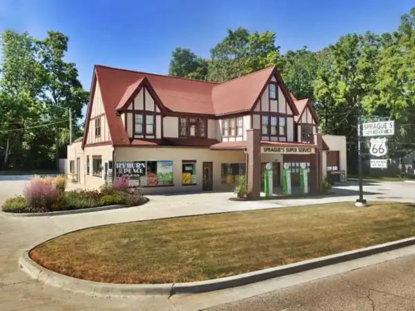 2-story, brick and wood, red gable roof Tudor mansion gas station, pumps under canopy with 2nd story gabled room, signs, paved drive, flowerbeds