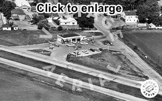 1965 aerial view Elwood Standard station black and white 1965 aerial photo. Route 66 four lanes runs bottom, Standard Oil gas station on an intersection with pumps and concrete drive area
