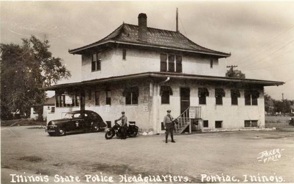 black and white 1930s two story hip roof building, police car, policeman standing and one on a motorcycle seen from US66