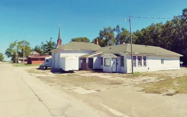 color, white woodframe building, hip roofed, to the right, City 66 to the left, church behind