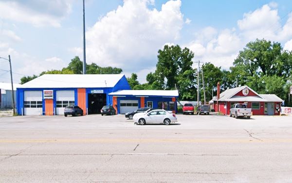 two buildings one with service bays, the other with a gable roof with a parking area facing Route 66