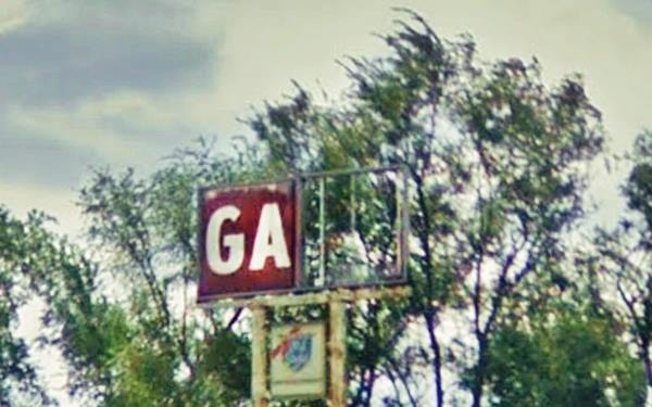 a broken faded old neon sign letters GA of GAS visible, tree and blue sky beyond