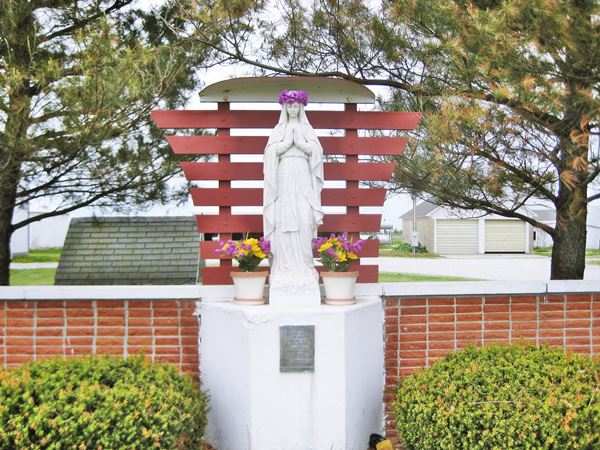close up of the statue of Our Lady of the Highways statue with a crown of flowers, brick pedestal with flower pots