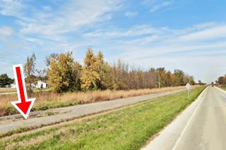 cracked concrete slabs of former Southbound lanes seen from current Frontage Rd (former northbound lanes), grassy median, trees beyond