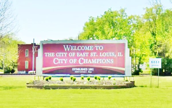 green lawn in a park with a red billboard with the words "Welcome to the city of East St Louis. IL City of Champions" written in white letters