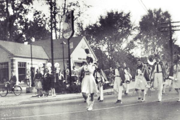 black and white photo 1940s parade and behind them gas station with Mobil sign