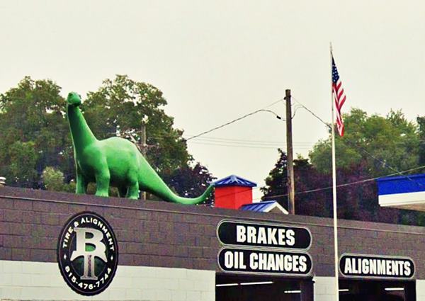 large sized fiberglass green dinosaur on the roof of a tire shop