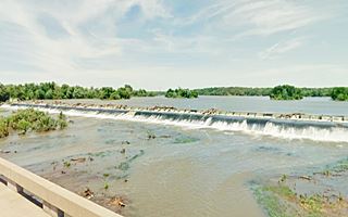 Riverton dam water spilling oer dam, trees, wide river