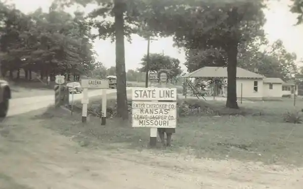state line at Galena on US66 c1940s 1940s view: trees, road, homes, a woman by the KS-MO state line sign