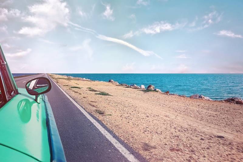sea shore and blue ocean seen from the window of a vintage green color car on a highway