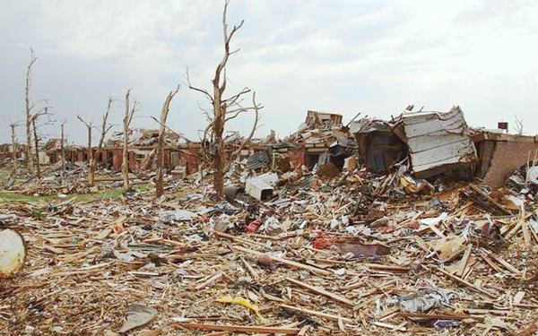Tornado devastation debris, timber, parts and pieces of buildings strewn and piled high on the ground, stripped tree