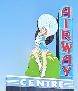 female parade leader or majorette with tall hat and boots and spinning baton neon sign with words Airway in red letters in blue sqares on the right