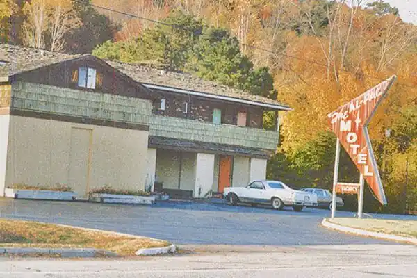 motel with red angular neon sign and 1970s car