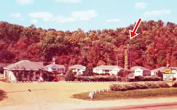 cabins with gravel driveway, wooded hill behind, neon sign
