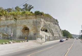 bluff with hole in it rises over Route 66 running at its foot, car, 2020s