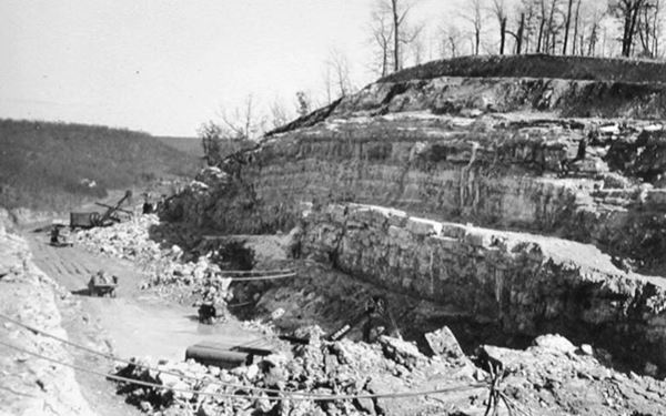 black and white photo, trucks and men excavating cut in hill
