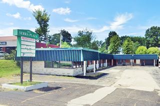 L-shaped flat roofed former motel now a shopping plaza with a neon sign