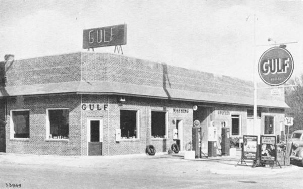 black and white vintage postcard of 1930s brick Gulf gas station and its pumps