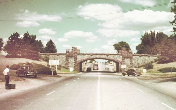 1940s color photo of highway, overpass ahead, cars, grass and trees on the shoulders