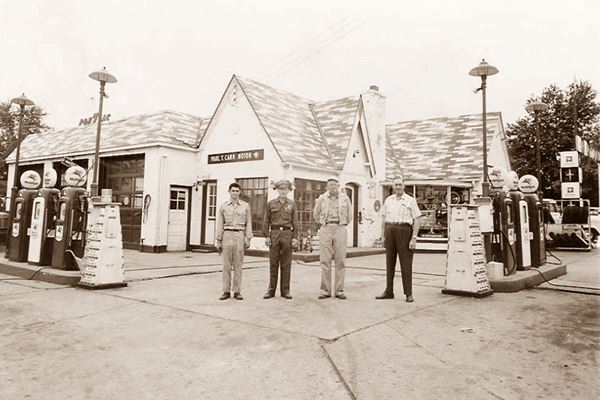 black and white photo c.1960 of a cottage style gas station with four men by the gas pumps