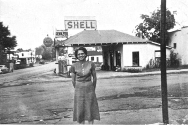 black and white 1950s postcard, hip roof gas station, woman, highway and Shell sign