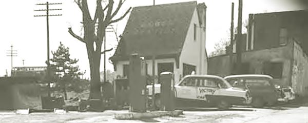 cottage style gas station with pumps and cars c.1950s