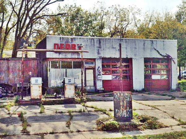 old vacant oblong-box gas station with white tiles and two garage bays and old 1970s gas pumps