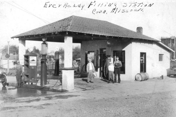 black and white 1930s postcard, hip roof gas station, men, gas pumps and signs