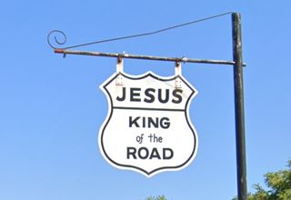 hW highway shield with "Jesus King 
of the Road" written on it with black letters