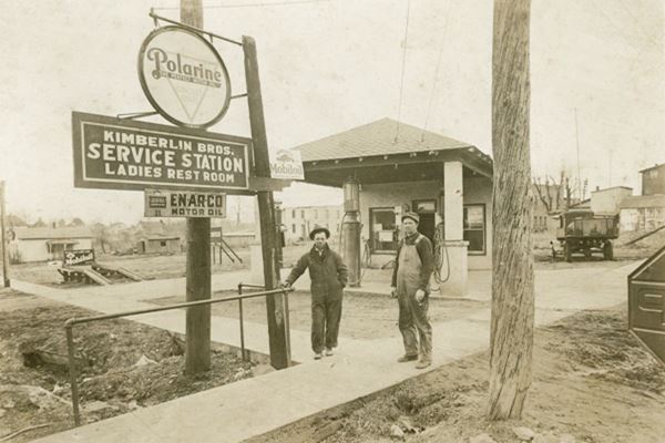 sepia 1930s postcard, hip roof gas station, two men, gas pumps and signs