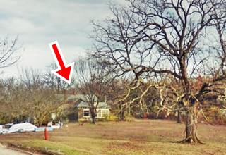 gable roof home among trees, with lawn and gavel entrance seen from Route 66