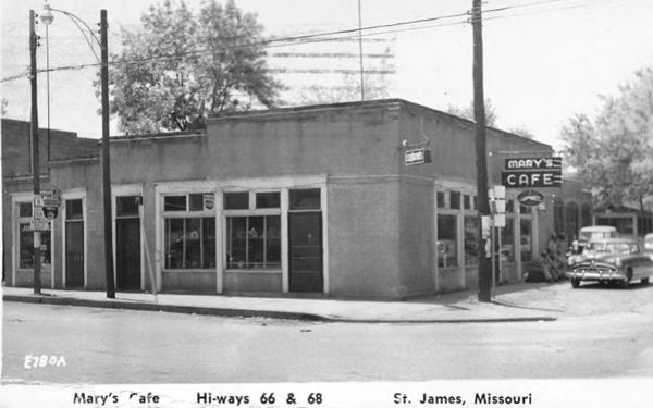 black and white photo c. 1950s of one story stucco walled corner building and a 1950s car, a bar on Route 66